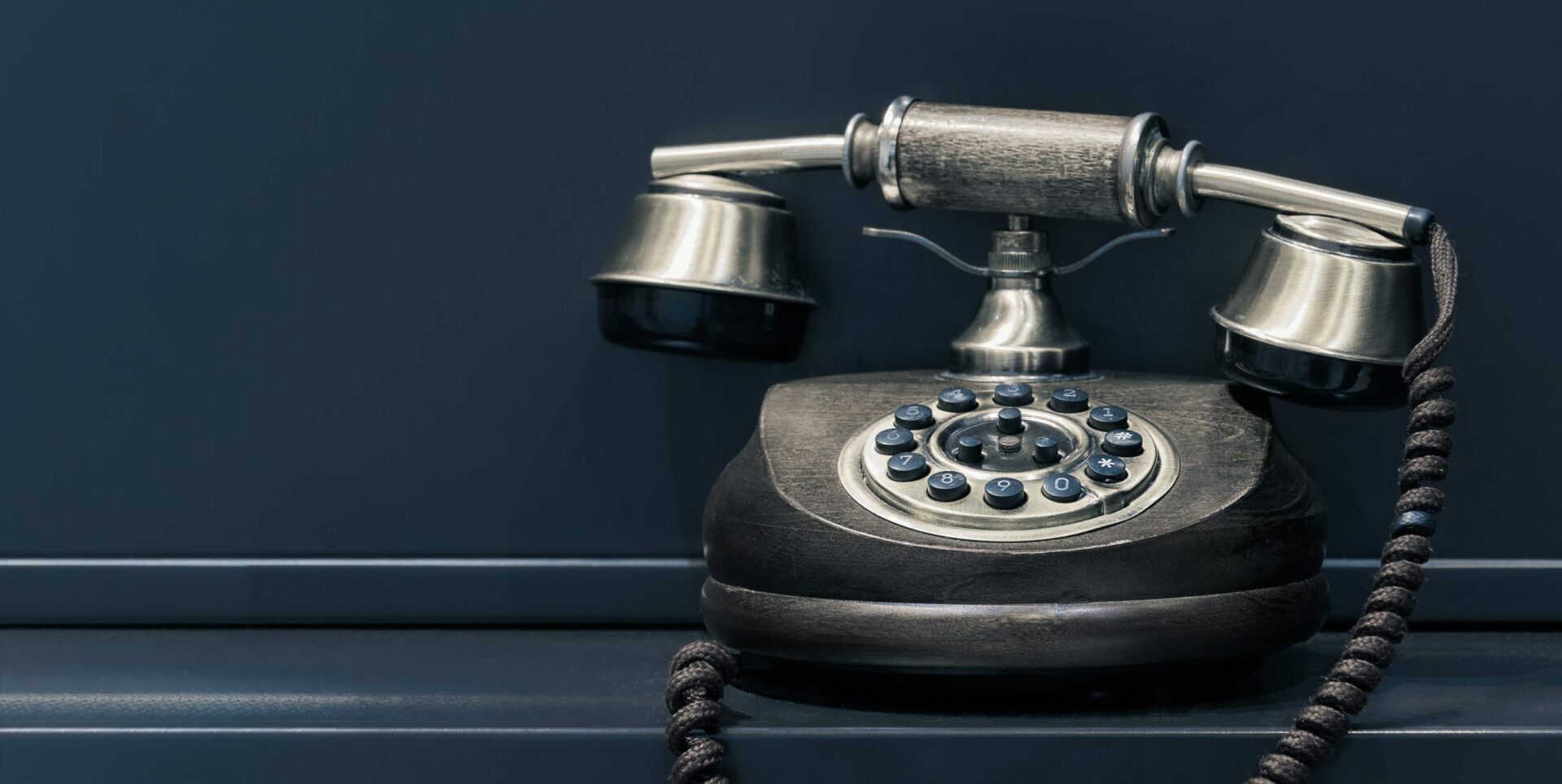 An old style black phone on a dark blue background